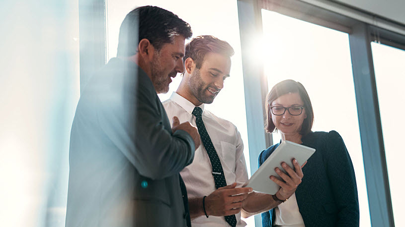 three coworkers reviewing information on a tablet three coworkers reviewing information on a tablet