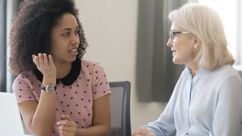 A younger woman and an older woman sit at a table and talk.