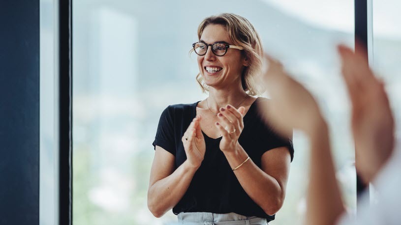 Career Paths A businesswoman stands and claps with others in an office.