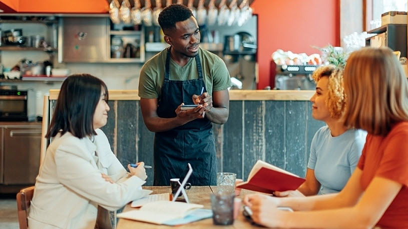 Young male waiter takes food orders at table of women 7 Ways to Turn Employee Schedules into a Hiring & Retention Asset