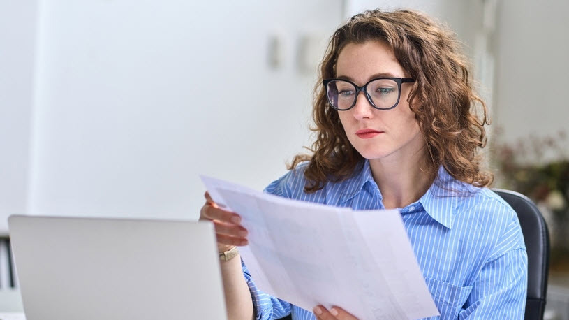 A woman at an office desk looks at papers.