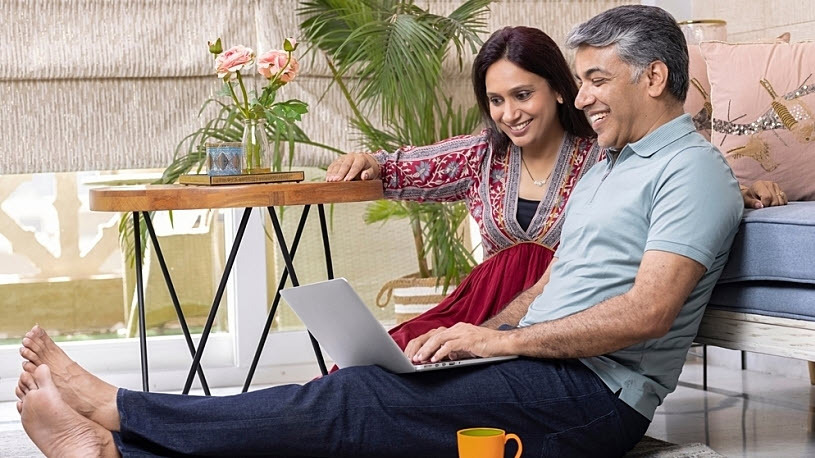 A middle-aged couple sits on rug with laptop planning retirement A middle-aged couple sits on rug with laptop planning retirement