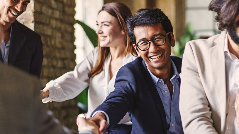 Inclusive Leadership A group of businesspeople shake hands with each other in an office.