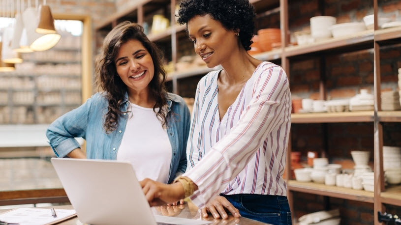 Small Business Accountant Services Two women stand at a counter with a laptop in a shop and discuss small business accountant services.