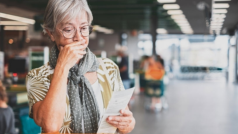 Senior woman frowns looking at grocery store receipt Senior woman frowns looking at grocery store receipt