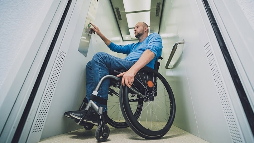 Inclusive Design Man who uses a wheelchair pushes button in wheelchair lift elevator