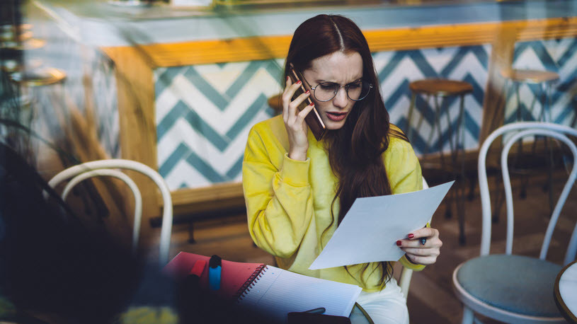 Female business owner talking on phone reads insurance claim Female business owner talking on phone reads insurance claim