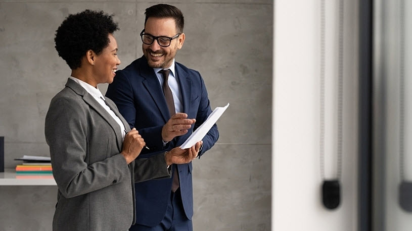 How to Design a Competitive Compensation Plan Smiling manager walking with employee showing compensation info on paper
