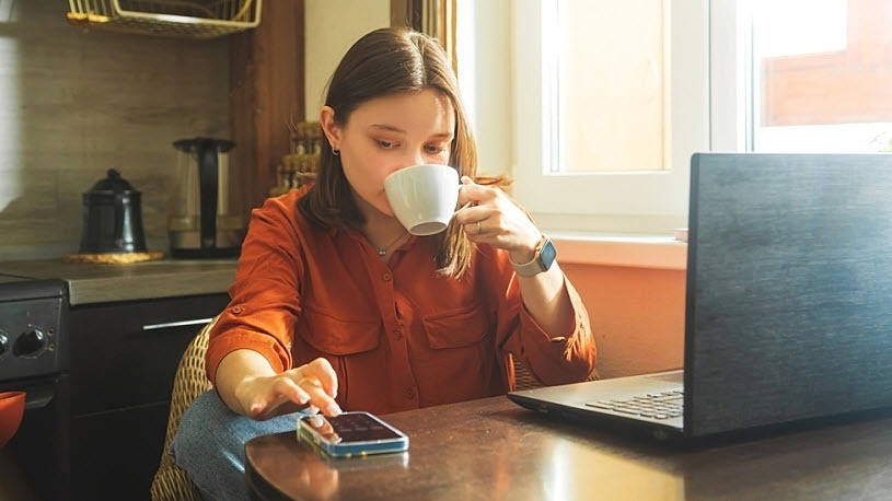 Hybrid Work Schedule A caucasion brunette woman at work at home office space with laptop checks mobile phone