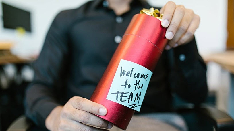How to Design an Onboarding Process That Drives Employee Success A person holding a present with a welcome note.