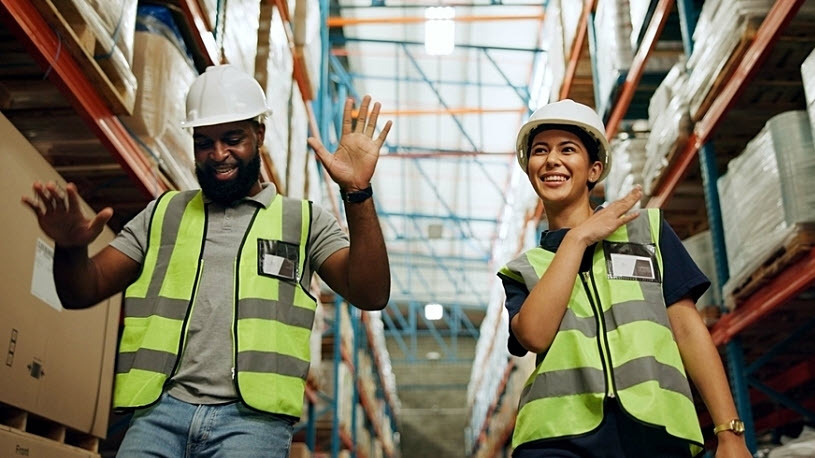 Happy young woman and man joking as they learn new skills at work Happy young woman and man wearing safety equipment in distribution warehouse joke with one another