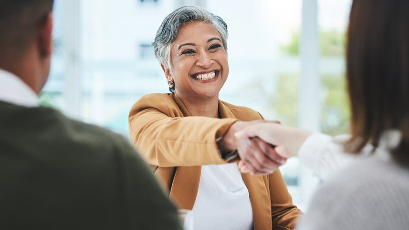 Smiling mature woman reaching across desk shaking hands Smiling mature woman reaching across desk shaking hands with two interviewers
