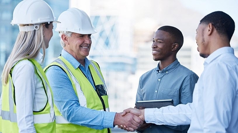 Managing talent in the 2025 construction industry Two construction officials speak with building representatives and shake hands.