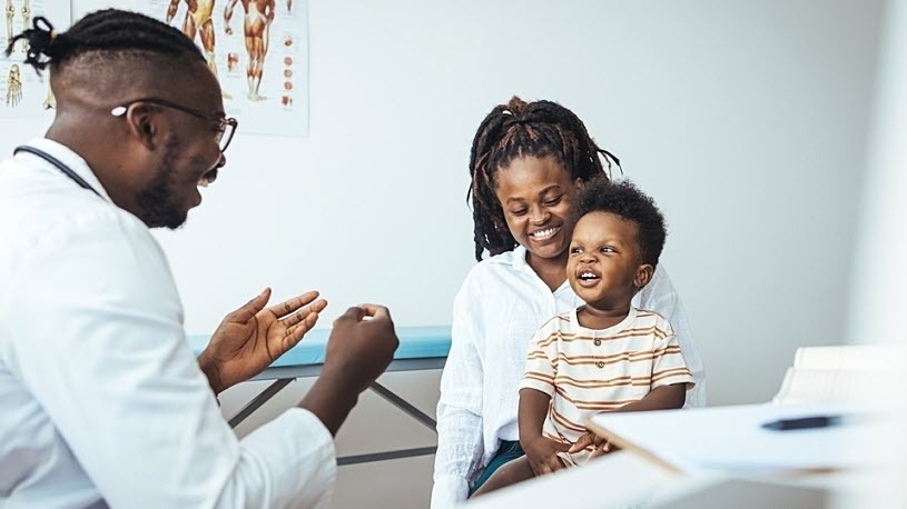 A boy sitting on his mother's lap in exam room smiles at doctor A boy sitting on his mother's lap in exam room smiles at doctor