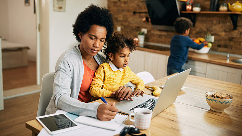 Working mother with child in lap taking notes and working at home Working mother with child in lap taking notes and working at home kitchen table