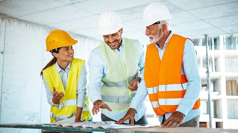 HR compliance for construction firms is becoming complex Construction workers collaborating and discussing construction plans at a work site.