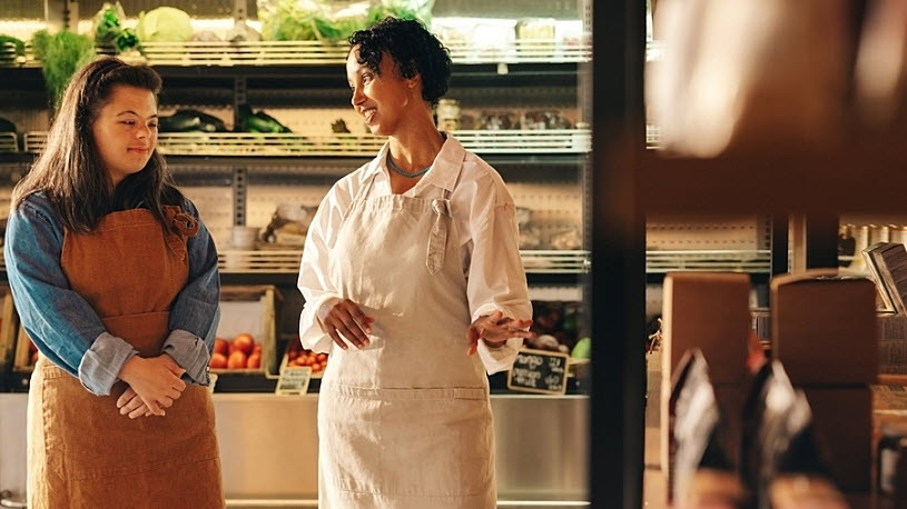 Grocery store manager talks with new employee while working Grocery store manager talks with new employee while working