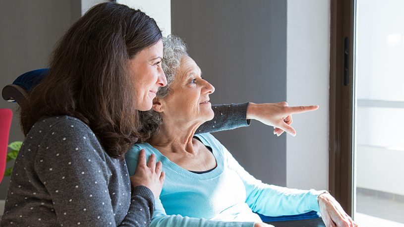 woman kneeling beside aging mother looking outside woman kneeling beside aging mother looking outside