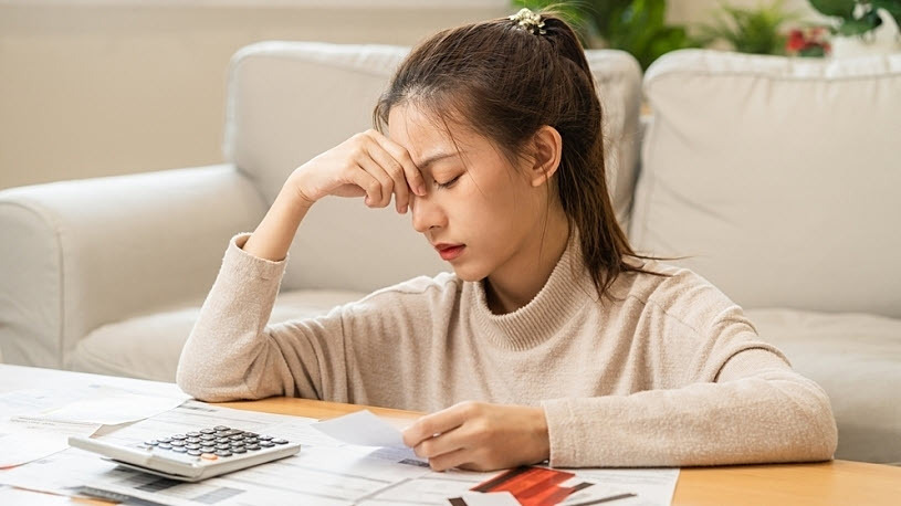 Young woman at home with hand to head worried about finances Young woman at home with hand to head worried about finances