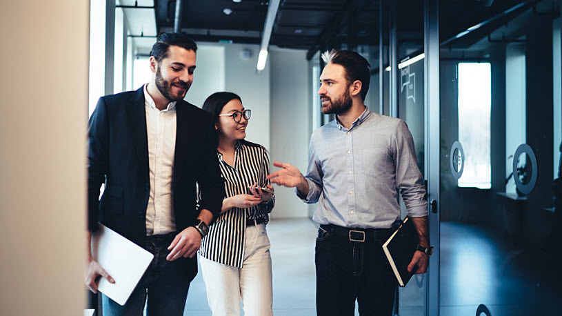 Three professionals talking about SUI tax rate management Diverse team of managers walking in office hallway discussing SUI tax rate management