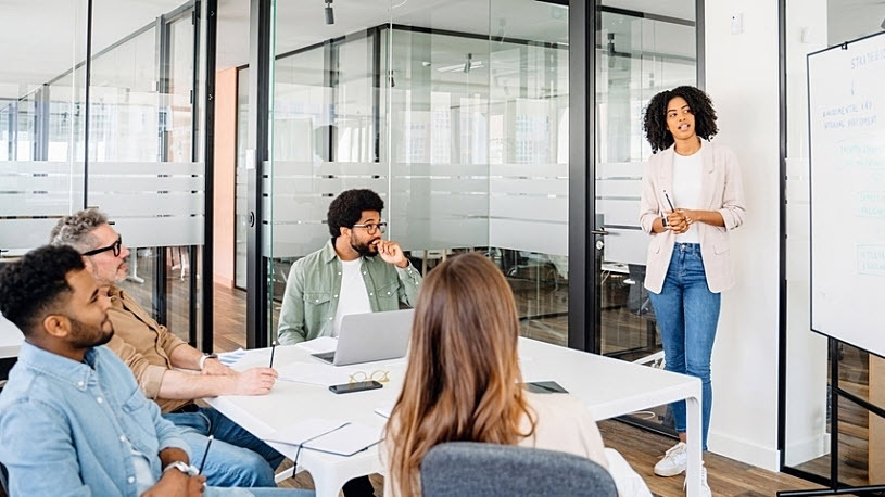 A professional woman stands presenting staffing options to team A professional woman stands presenting staffing options to team