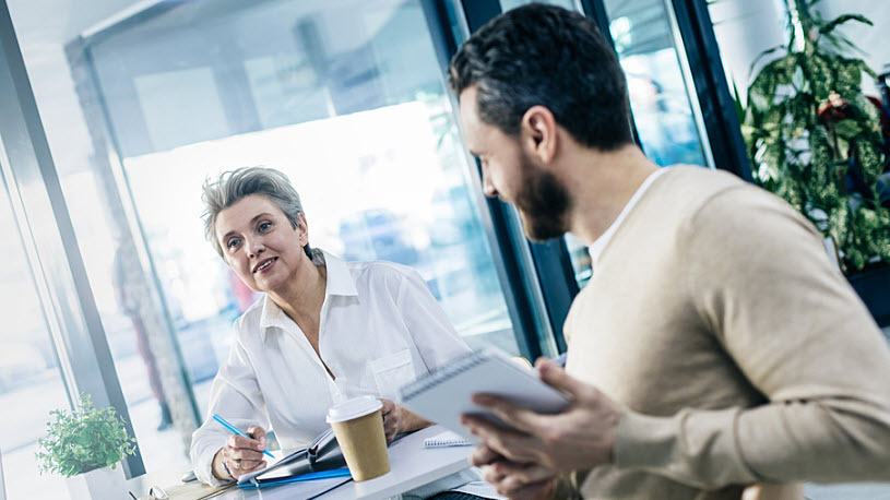 Cheerful mature woman leader smiling with team member at table