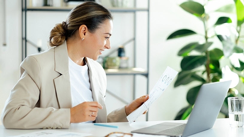 A smiling businesswoman sits at a desk reviewing year-end reports