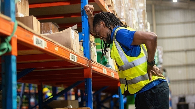 Warehouse worker experiencing back pain standing on ladder