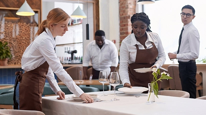 Ethnically diverse wait staff working to prepare restaurant table