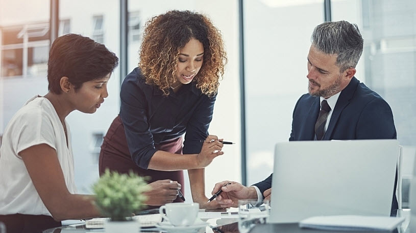 Three HR and data leaders talk and gesture at a planning meeting at a conference room table