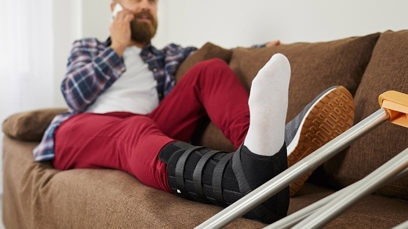 close-up of man with foot in cast and crutches sits on couch