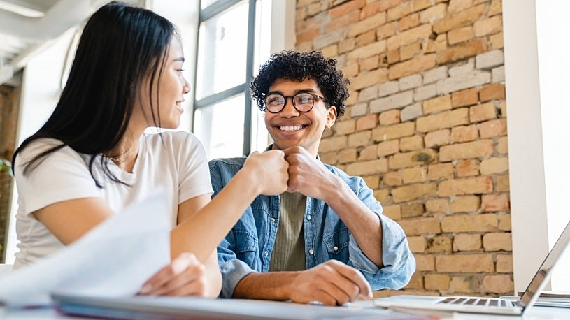 Smiling young business partners giving a fist bump while working Smiling young business partners giving a fist bump while working