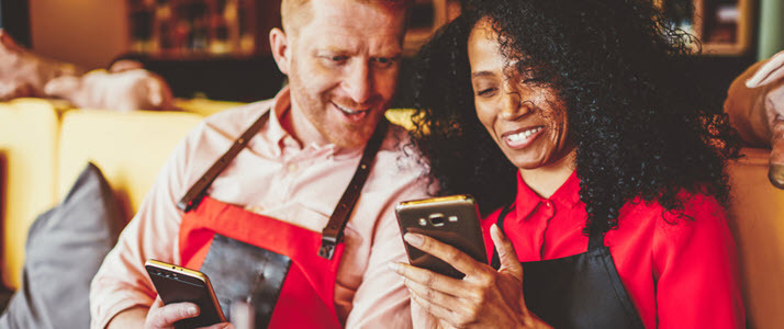 Faster Payments Can Benefit You and Your Workforce Two workers smile as they access their wages on mobile devices