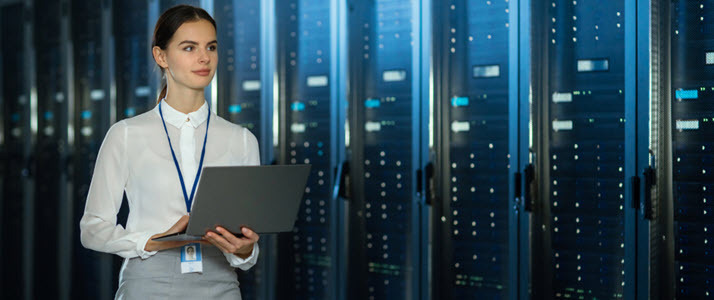 Data center female employee with laptop walking among servers