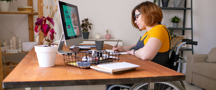 Woman in wheelchair writing at desk with computer