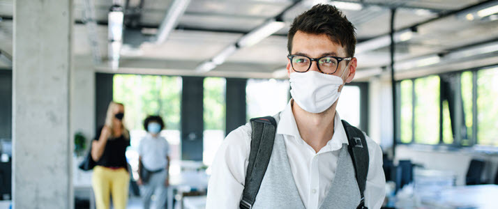 Young man with face mask walking into office