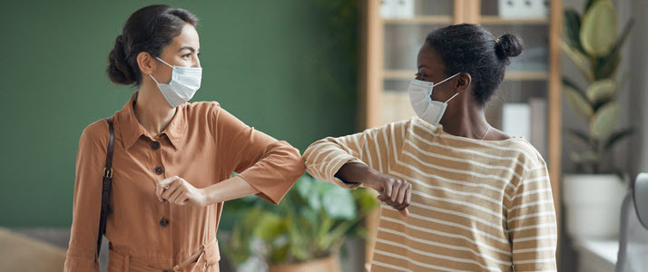 two female coworkers in masks elbow bump greeting
