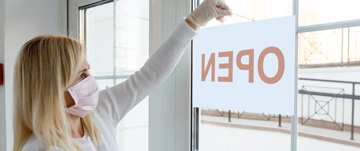 business owner posting open sign wearing mask