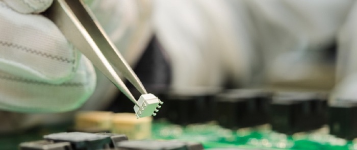 Digicom Electronics A 15-Year Partnership Lifts the Bottom Line A hand holding tweezers manipulates electronic components.