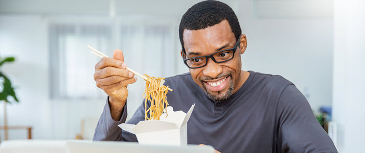 African American man eating noodles at desk