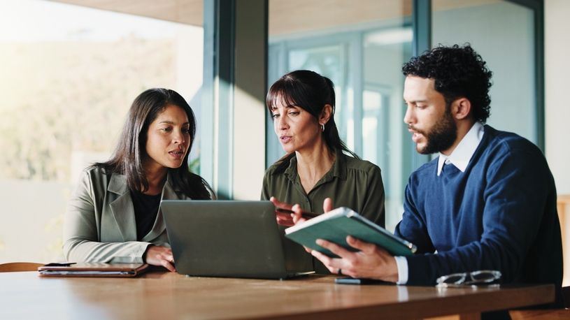 Three professionals collaborating around a laptop