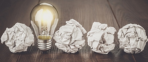 An image of a lightbulb, along with several pieces of crumpled paper, lined up on a table.