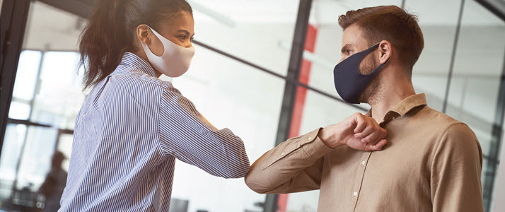 Masked coworkers touching elbows in the office