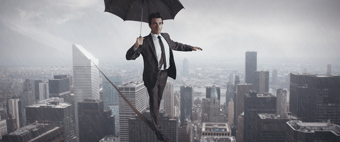 A businessman walks on tightrope between skyscrapers in the rain.
