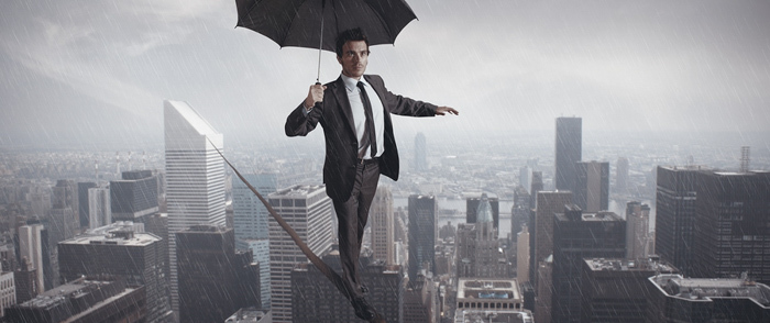 Employee Motivation A businessman walks on tightrope between skyscrapers in the rain.
