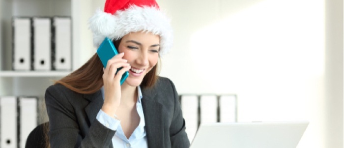 A business woman speaks on a cell phone while wearing a festive holiday hat.