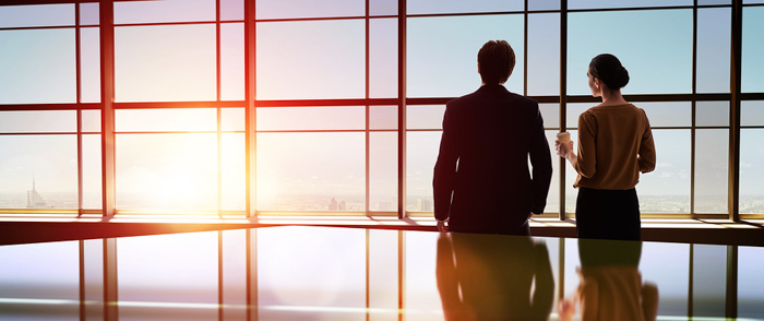 Manager Relationships Two colleagues stand together in an office and watch the sunset.