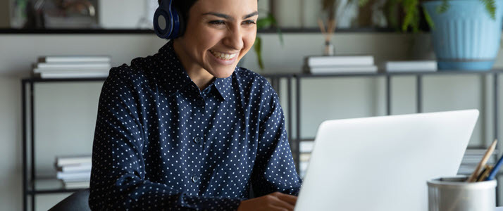 Woman using her laptop for a video call Young woman with a blue shirt wearing headphones and using her laptop for a video call