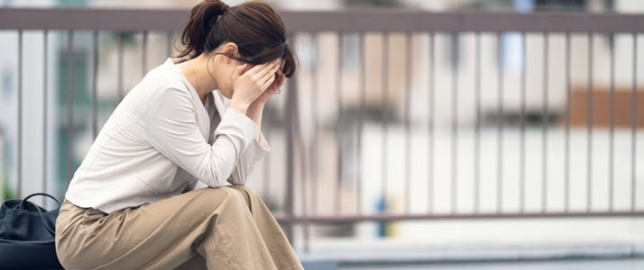 Asian woman with head in hands sitting outside