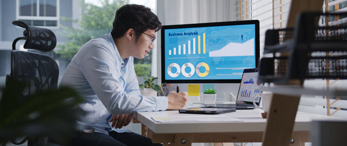 young man at desk with computer screen showing charts